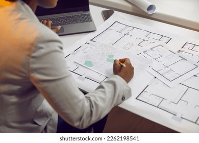 Female architect sitting at her office desk and working with blueprints, cadastral maps and city plans. Young African American woman studying information and developing a new architectural project - Powered by Shutterstock