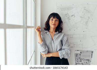 Female Architect Standing In Office Beside Architecture Drawings. Woman Entrepreneur Standing In Office Making Presentation.