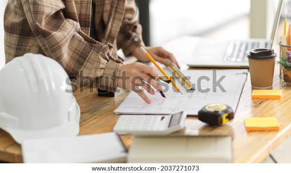 Female architect using divider\
compass to measuring layout building in engineers office, hardhat,\
calculator, measurement, architect equipments on\
worktable