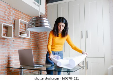 Female architect working at home with a laptop and blueprints. Persian woman designing a project. - Shutterstock ID 1606784521