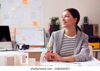 Female Architect Working In Office With Model On Desk Studying Plans For New Building