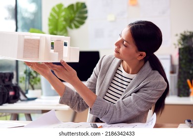 Female Architect Working In Office Studying Model Of New Building