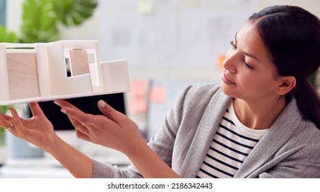 Female Architect Working In Office Studying Model Of New Building