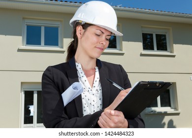 Female Architect Writing On Clipboard Outside Of Residential Property