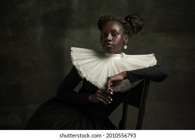 Female aristocrat with white pearl. Medieval African young woman in black vintage dress with big white collar isolated on dark green background. Concept of comparison of eras, modernity and