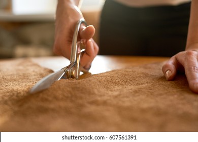 Female artisan cutting brown leather with scissors close up