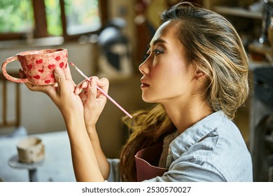 Female artist decorating and painting handmade ceramic clay cup at her creative workshop. Artwork and handmade concept - Powered by Shutterstock