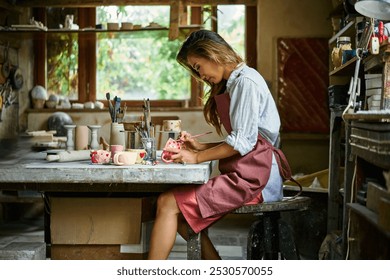 Female artist decorating and painting handmade ceramic clay cup at her creative workshop. Artwork and handmade concept - Powered by Shutterstock