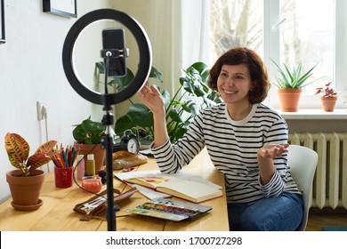 Female artist filming design workshop at home for online education. Working from home making master-class using ring lighting. Cozy artist's studio. 