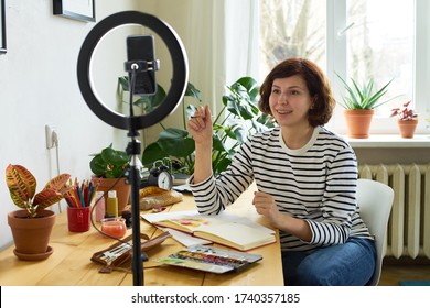 Female artist filming design workshop at home for online education. Working from home making master-class using ring lighting. Cozy artist's studio. 