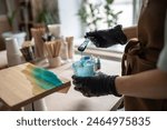 Female artist pours epoxy resin and smears it with stick on wooden board. Craftswoman creating picture of sea and waves, closeup view. Art deco, handmade, master class on resin art. 