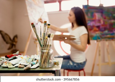 Female Artist Working On Painting In Studio. Background image, selective focus on  foreground