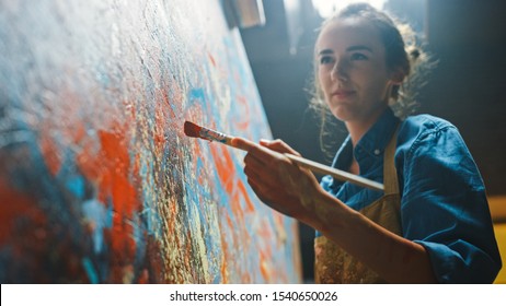 Female Artist Works on Abstract Oil Painting, Moving Paint Brush Energetically She Creates Modern Masterpiece. Dark Creative Studio where Large Canvas Stands on Easel Illuminated. Low Angle Close-up - Powered by Shutterstock