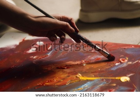 Female Artist Works on Abstract Oil Painting, Moving Paint Brush Energetically She Creates Modern Masterpiece. Dark Creative Studio where Large Canvas Stands on Easel Illuminated. Low Angle Close-up