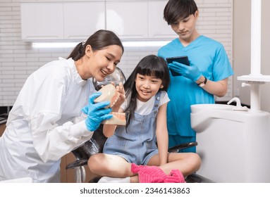 Female asain dentist holding tooth model and talking to child in dental clinic.SHOTLISThealth - Powered by Shutterstock