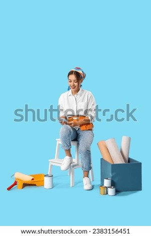 Female Asian decorator with paint color palettes sitting on blue background