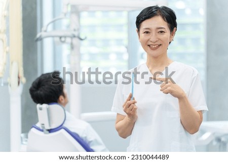 female asian dentist showing toothbrush in dental clinic