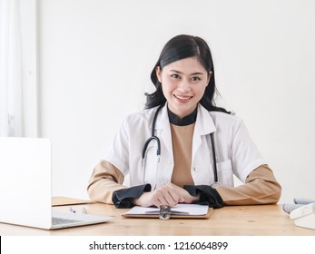 Female Asian Doctor Working At Office Desk And Smiling At Camera.