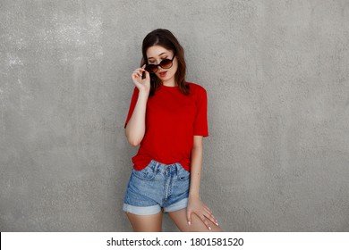 Female Asian Hipster Wearing Blank Red T-shirt And Denim Shorts Posing Against Rough Street Wall, Minimalist Urban Clothing Style, Mockup For Tshirt Print Store