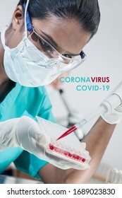 Female Asian Indian Medical Scientist Researcher Or Doctor Wearing A Face Mask Testing Coronavirus COVID-19 Blood Sample In A Laboratory With Her Colleague