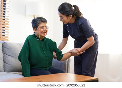 Female Asian Nurse Help Old Lady Stand Up From A Couch.