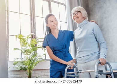 Female asian nurse helping senior woman to walk with walker at home. Rehabilitation after injuries, traumas, walking disability and movement impairment. Senior life concept - Powered by Shutterstock