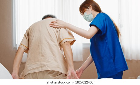 Female Asian Nurse Support Senior Male Patient Stand Up And Walk From Bed In Hospital. Nursing Home, Medical Service, Physiotherapy, Hospitality, Or Recovery Treatment Concept