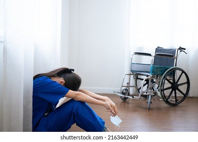 Female asian nurse wears face mask blue uniform sits on hospital floor. Depressed sad Thai ethic doctor feels fatigue burnout stress, lack of sleep, napping at work.Tired exhausted people. - Shutterstock ID 2163442449