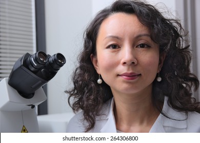 Female Asian Scientist With Microscope Behind Her