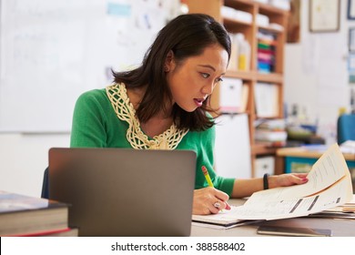 Female Asian Teacher At Her Desk Marking StudentsÃ¢?? Work