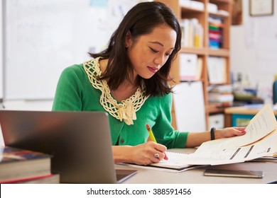 Female Asian teacher at her desk marking studentsÃ¢?? work
