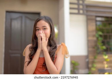 A Female Asian Teenager Covers Her Mouth In Surprise When She Heard The Shocking News. Outdoor Scene Outside The House.