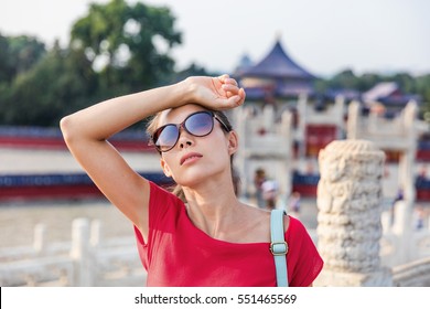 Female asian tourist exhausted during famous attraction visit vacation. Woman wearing sunglassses sweating from sun and heat exhaustion on warm summer day in Beijing, China. Asia travel destination.