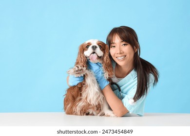 Female Asian veterinarian with cute dog on table against blue background - Powered by Shutterstock