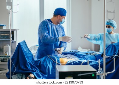 Female Assistant Nurse Help Surgeon Preparing The Patient For Surgery. Operation Under General Anesthesia. Modern Surgery Room. Real Photo In Operating Room.