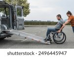 Female assistant pushing a man with disability, a wheelchair user up the car ramp into the van. Accessibility and travel concepts.