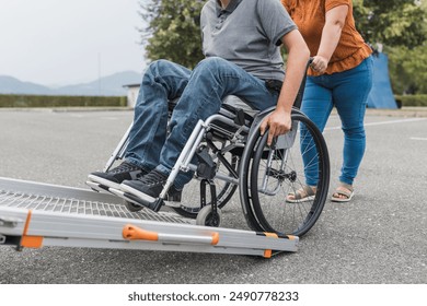 Female assistant pushing a man with disability, a wheelchair user up the car ramp into the van. Accessibility and travel concepts. - Powered by Shutterstock