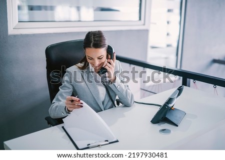 A female assistant schedules a business meeting on the phone at corporate firm.