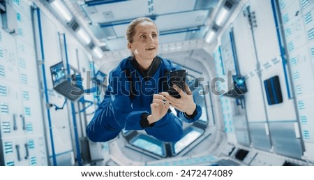 Female Astronaut Floating in Zero Gravity Inside a Space Station. Spacewoman Using Smartphone in Space in Orbiting Spacecraft, Browsing Internet Content, Checking and Updating Social Media Networks