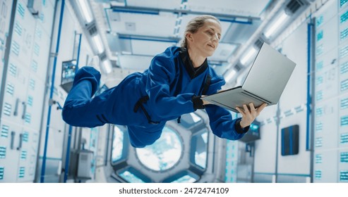 Female Astronaut Using a Laptop Computer in Space Inside a Spacecraft. Working Online, Checking and Updating Flight Information, Writing Report. Spacewoman Floating in Zero Gravity Inside a Spaceship - Powered by Shutterstock