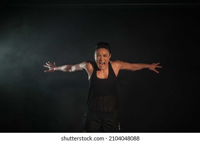 Female Athlete With Arms Out Wide Lunging Forward Screaming With Dark Moody Background