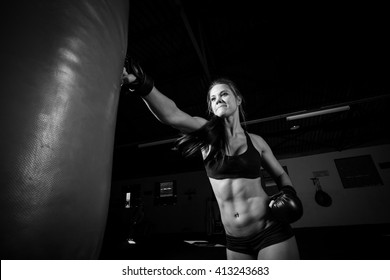 Female Athlete Boxer Punching A Punching Bag With Dramatic Edgy Lighting In A Dark Studio