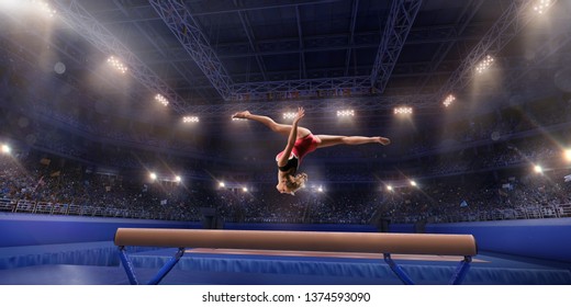 Female Athlete Doing A Complicated Exciting Trick On Gymnastics Balance Beam In A Professional Gym. Girl Perform Stunt In Bright Sports Clothes