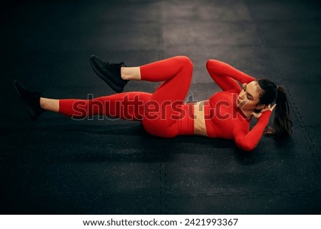 A female athlete is doing knee to elbow crunches on a gym floor.
