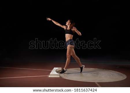 Female athlete doing a shot-put throw, black background.