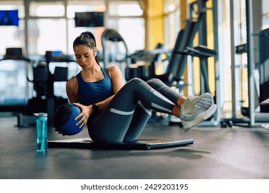 Female athlete doing sit-ups with medicine ball while working out in health club. - Powered by Shutterstock