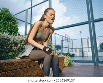 Female athlete experiencing discomfort while resting outdoors near a basketball court against a sunny sky - Powered by Shutterstock