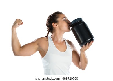 Female athlete flexing muscles while kissing supplement jar while standing against white background - Powered by Shutterstock