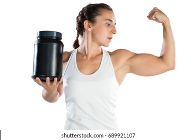 Female athlete flexing muscles while holding supplement jar against white background - Powered by Shutterstock