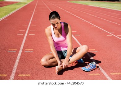 Female athlete with foot pain on running track on a sunny day - Powered by Shutterstock